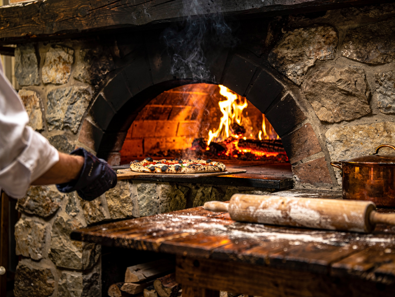 Flames roaring in wood-fired oven while chef tends to charred specialties